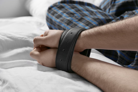 Male hands tied up with belts in bed