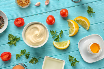 Mayonnaise in bowl with ingredients on wooden background, top view