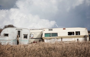 horizontal image of old wrecked holiday campers sitting in the junk yard under a dark cloudy sky in the spring.