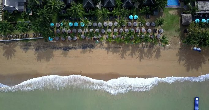 Aerial footage of a tropical beach with waves and a couple walking on the beach, panning out above view. Summer vacation holiday.
