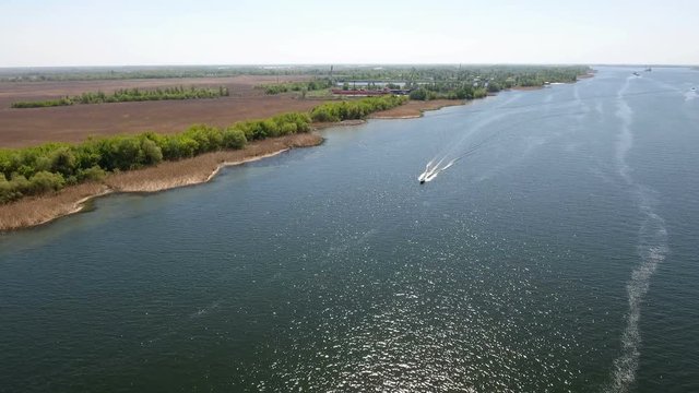Amazing aerial shot of the Dnipro river with its little islets, curvy hook with indented coastline, straw looking grass, patches of greenary, motorboat, and superb skyscape in Ukraine in a sunny day