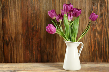 Vase with beautiful bouquet of lilac tulips on table against wooden background