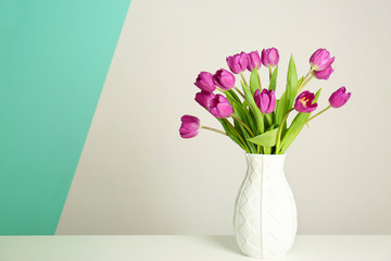Vase with beautiful bouquet of lilac tulips on table against light background