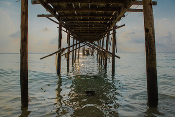 Old wooden bridge in the sea at morning time .