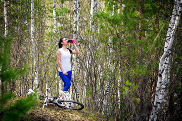 A woman in a wild forest drinks from a bottle. Pine, birch, bicycle