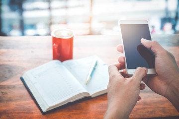 Young businessman hands using mobile smartphone with red coffee cup. Businessmen working at coffee shop (cafe) with mobile smartphone and note book. Vintage color filter..