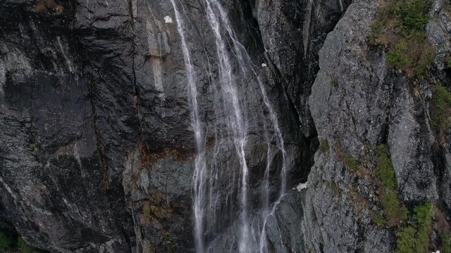 Aerial of Fresh Winter Snow Melt trickling Down Big Mountain Rock Cliff Face in Spring Season 