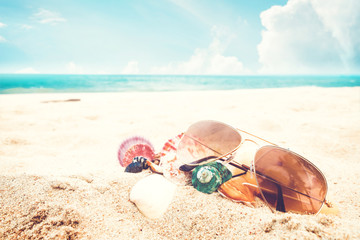 Sunglasses and seashell on the sandy tropical beach with clear blue sky. Leisure in summer and Summer vacation concept. vintage color tone.