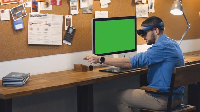 Young adult Caucasian male using holographic augmented reality glasses, creating a model on a computer screen. Green screen chroma key. 4K UHD RAW edited footage