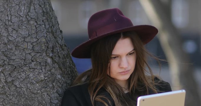 Pretty smiling hipster girl relaxing in the park and using tablet. 4k, steadicam