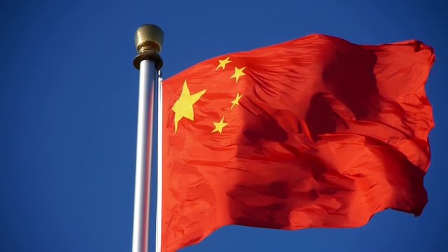 Chinese red flag flutters in wind & blue sky.