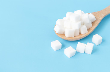 Closeup sugar cubes on wooden spoon white blue background