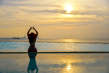 Woman in big hat relaxing on the swimming pool, near the sea in the sunset