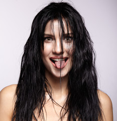 Portrait of a young brunette woman with moist long hair hairdo shows tongue