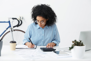 Portrait of attractive hardworking businesswoman with Afro hairstyle busy doing paperwork at office...
