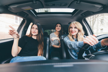 Three beautiful young cheerful women looking at away with smile while sitting in car