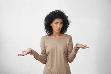 So what, Who cares. Unsure doubtful dark-skinned woman with black shaggy hair shrugging her...