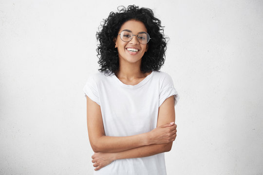 Youth and carefree lifestyle concept. Happy young woman freelancer with black curly hair relaxing at home after finished all work, having cheerful joyful look, keeping hands folded. Horizontal