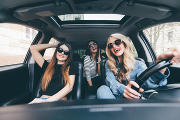 Three beautiful young cheerful women looking away with smile while sitting in car