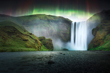 Green aurora light behind famous Skogafoss waterfall