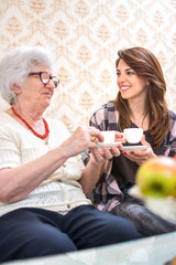 Grandmother and granddaughter sitting together beside table, talking and drinking coffee.