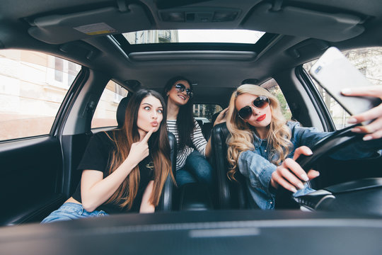 View of three beautiful young cheerful women making selfie and smiling while sitting in car together