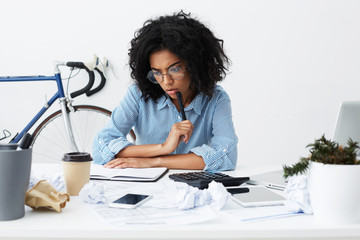 Concentrated female marketing expert holding pen, looking thoughtful while working over new...