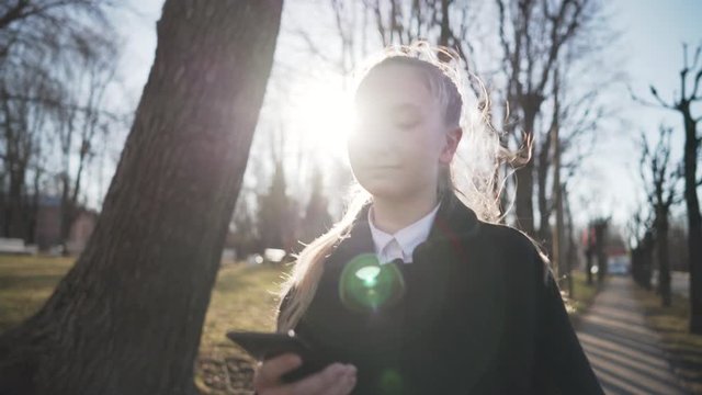 Gimbal shot of female teen girl using smartphone and walking in town in spring sunny day, uhd prores footage