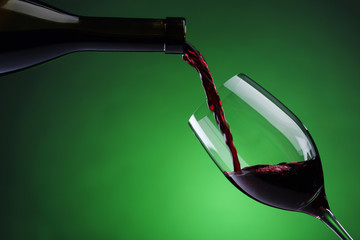 Pouring red wine into wine glass on green background © Vitalii Hulai