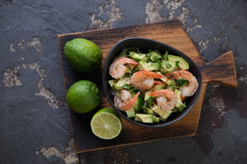 Salad with avocado, cucumber and fried tiger shrimps, top view on a dark brown stone background