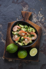 Above view of salad with avocado, tiger shrimps and cucumber on a dark brown stone surface