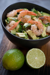 Close-up of avocado salad with fried tiger shrimps and sliced cucumber served in a bowl, studio shot