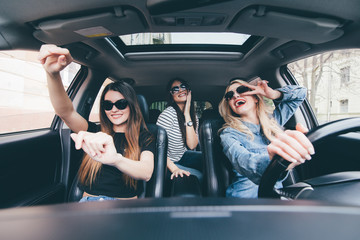 three girls driving in a convertible car and having fun, listen music and dance