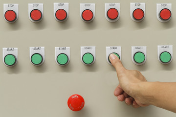 Thumb touch on green start button and red emergency stop switch. Control panel of automatic machine.