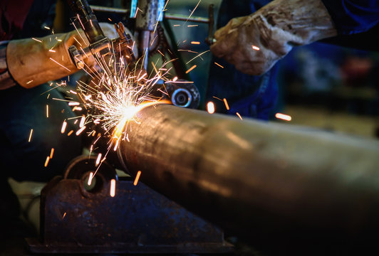 Worker cutting steel pipe with acetylene welding cutting torch and bright sparks in steel construction industry.