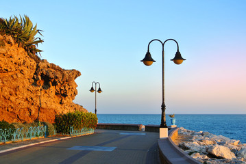 Promenade of Torremolinos, a road, rocks, blooming bushes and Mediterranean sea, Andalusia, Spain.