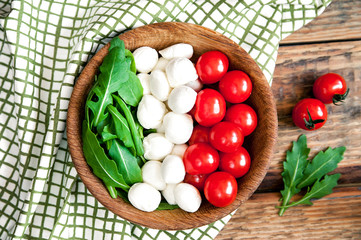 Flag of Italy from ingredients for vegetarian healthy salad - cherry tomato, mozzarella cheese and arugula on a wooden plate. Old dark wooden table background with napkin.