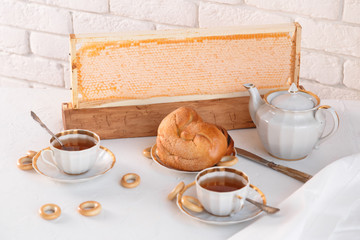 Cups of tea and teapot with honey and sweet buns over white brick background