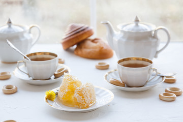 Cups of tea with honey on a plate and teapot, white baackground