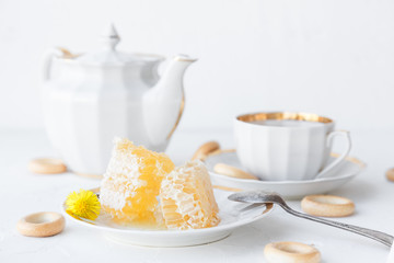 Cup of tea, teapot and honeycomb on a plate, withhoneycomb on background