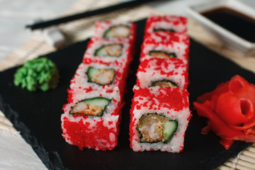 Appetizing delicious sushi rolls set with red tobiko served on black slate, close up. Japanese traditional and healthy food.