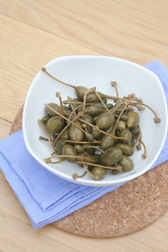 Frutti del cappero sott'olio in una ciotola su tavolo di legno