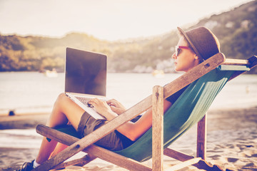 Young beautiful woman hipster traveler freelancer with laptop on the seashore. Business and...