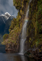 Close up of waterfall falling over a cliff into the sea with snow-capped mountains in the background, Doubtful Sound, New Zealand.