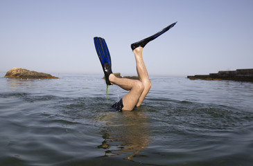 Feet of a diving man in black fins for swimming above the surface of the water against the backdrop of desert rocks