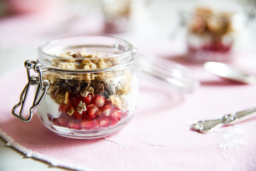 Diet dessert with yogurt, granola and pomegranates in a glassware. Horizontal. Rose tablecloth, silver spoon.