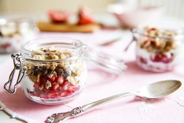 Diet dessert with yogurt, granola and pomegranates in a glassware. Horizontal. Rose tablecloth, silver spoon.