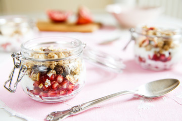Diet dessert with yogurt, granola and pomegranates in a glassware. Horizontal. Rose tablecloth, silver spoon.