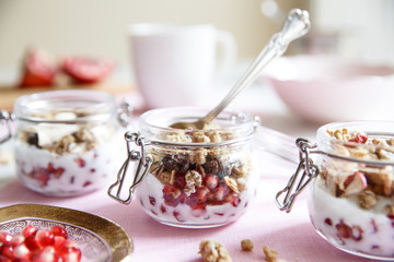Crunchy Yoghurt with fresh pomergranate (detailed close-up shot). Diet dessert with yogurt, granola and pomegranate in a glassware, horizontal. Three glass jars.