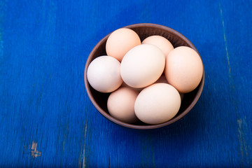 Fresh eggs in a brown bowl on  blue background. Top view